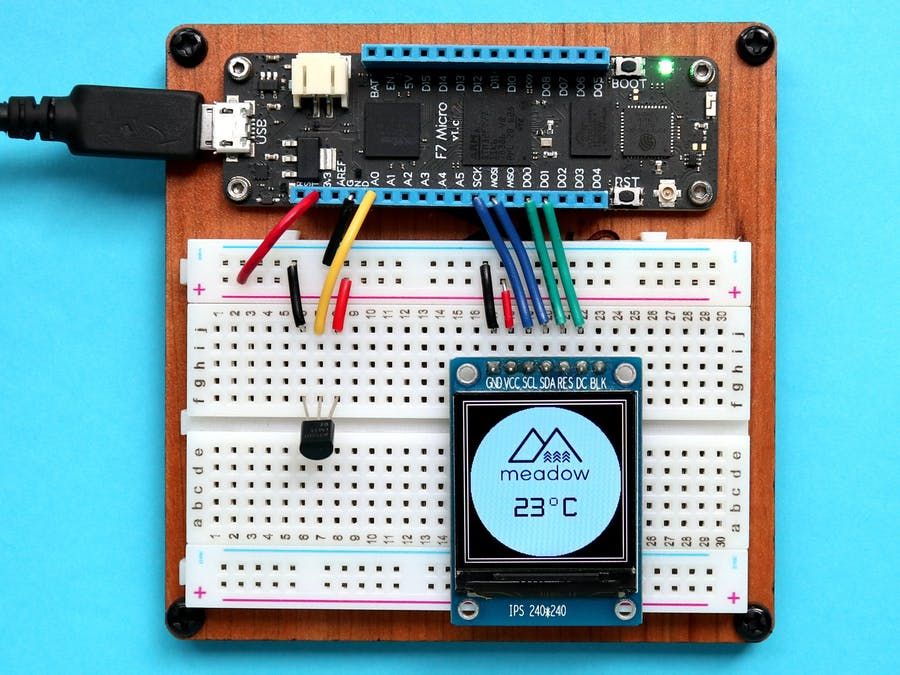 Photo of a Meadow board connected to a breadboard with a temperature sensor and 240-by-240 pixel display showing the Meadow logo and 23 degrees Celsius.