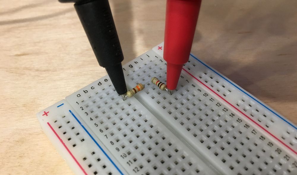 Photo of multimeter hook probes around the legs of two resistors to measure resistance across them both.