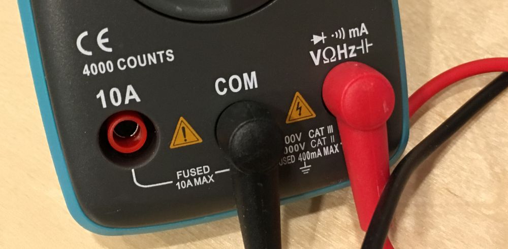 Photo of multimeter probes plugged in, black to COM socket and red to the V (volts) socket.