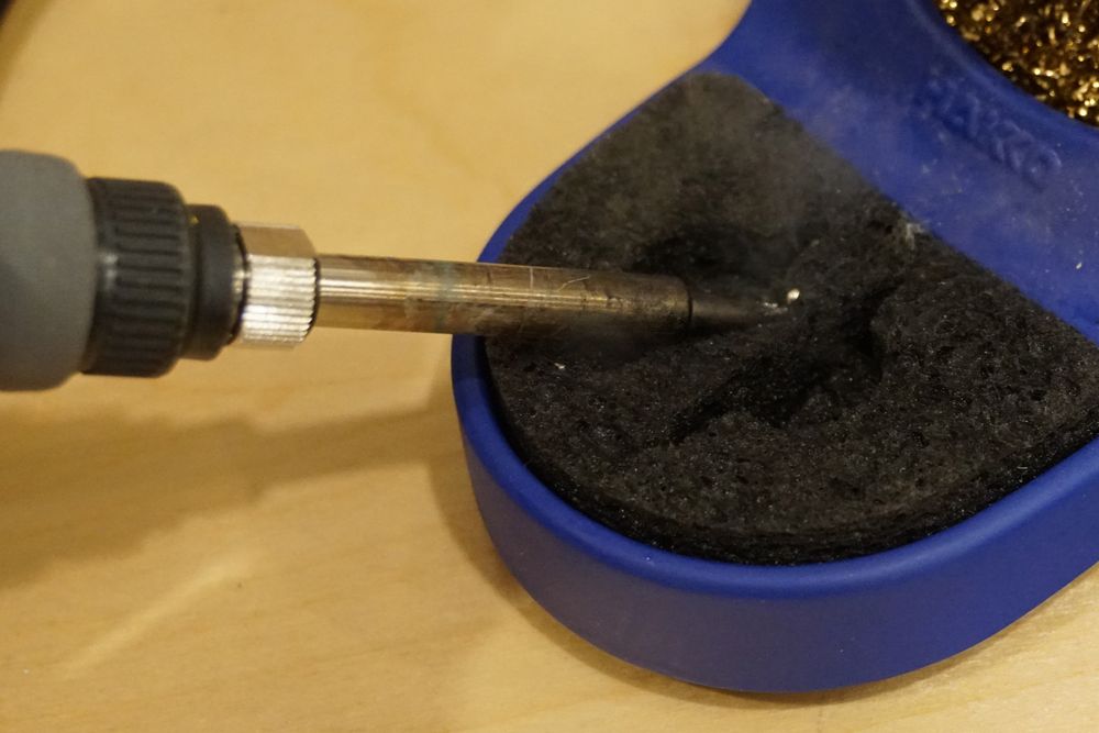 Photo of a soldering iron tip pressing into a wet sponge to remove excess solder.