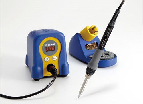 Photo of a Hakko Soldering Station with a blue and yellow base with temp display and adjustment buttons as well as a holder with brass mesh tip cleaner.