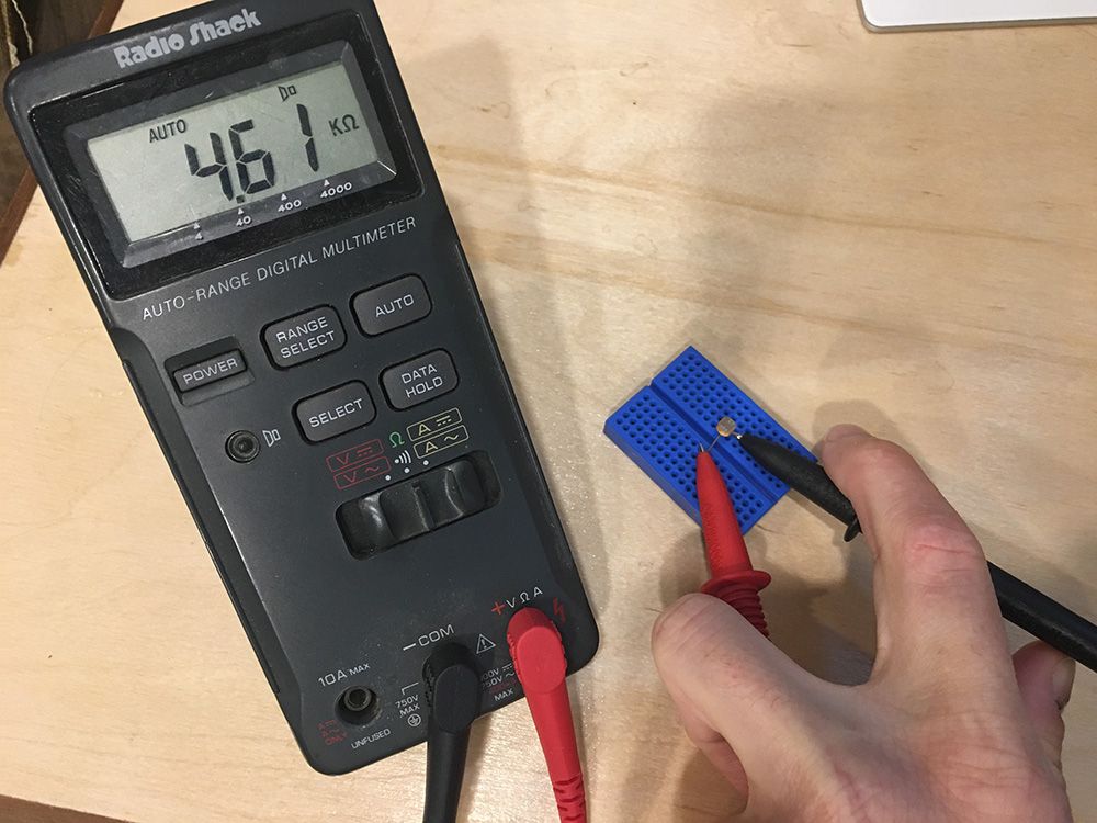 Photo of using a multimeter to measure resistance of a photoresistor mounted in a breadboard.