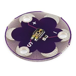 Photo of a LilyPad 5V Luminosity Sensor circular PCB with outer solder and hole attachments for connecting to wearable projects.