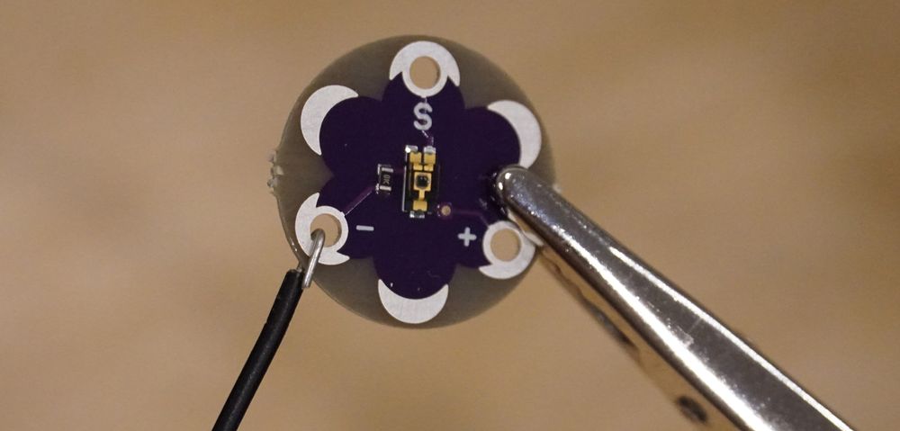 Photo of a sensor PCB held in place by an clip with a stripped jumper wire wrapped around one of the holes to make a connection.