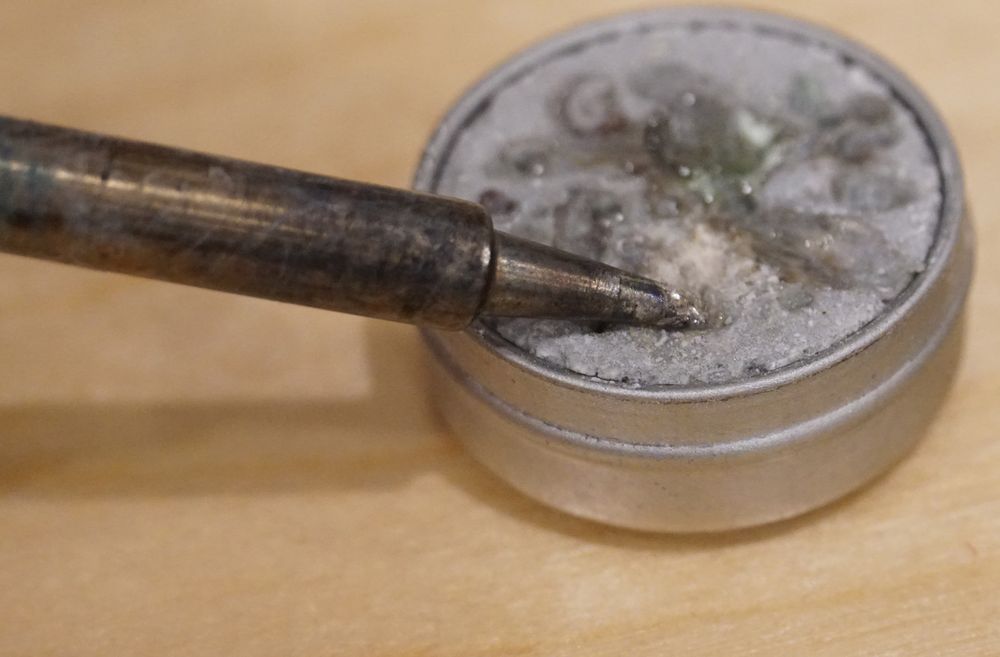 Photo of a soldering iron tip pressing into a metal can of tip tinner.
