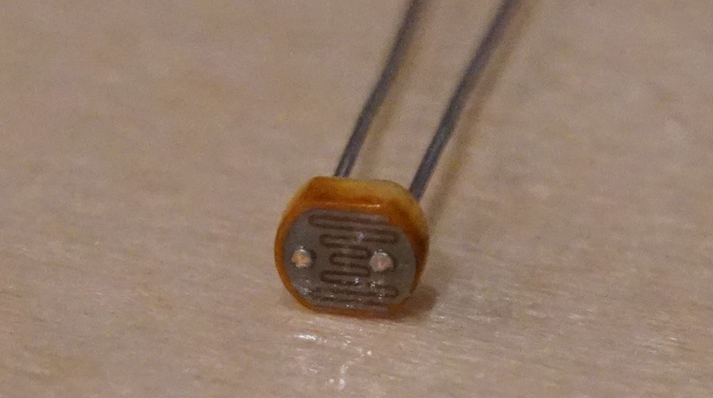 Photo of a photoresistor with a top flat disc sensor shape on top of two mounting legs. The sensor has two sides separated by a winding path back and forth between them.